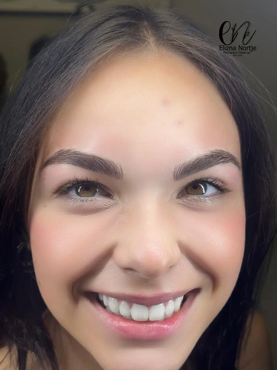Smiling woman showcasing natural beauty with permanent makeup.